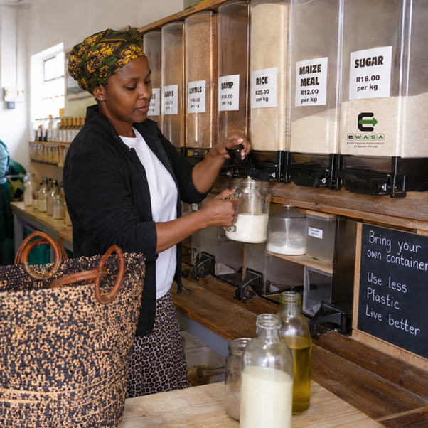 Shopper refilling basic groceries at a township refill store in South Africa using reusable containers to avoid single‑use packaging.
